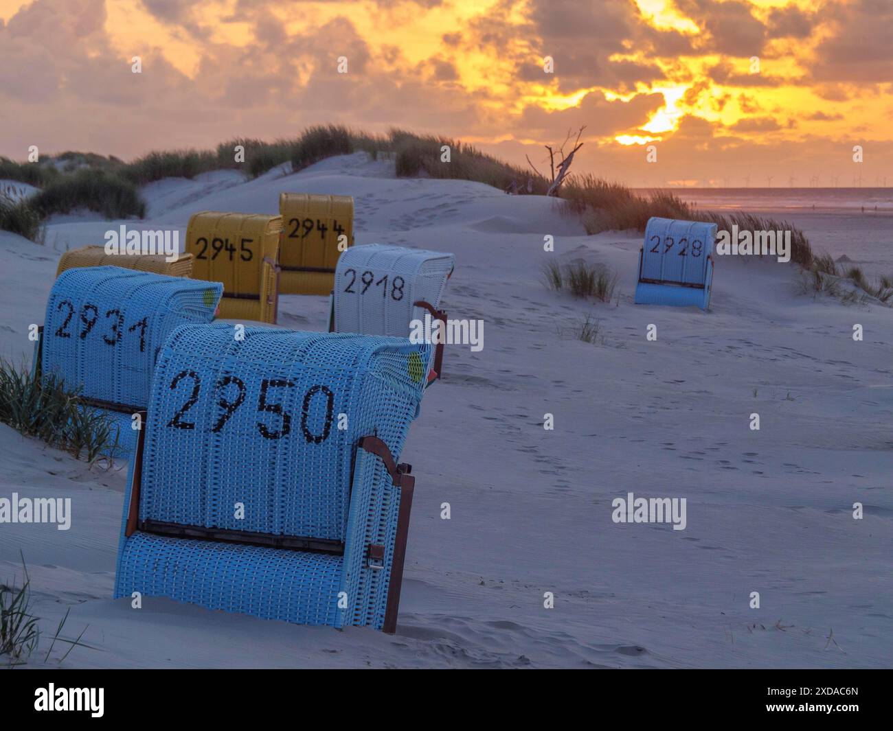 Several beach chairs stand in the dunes under a dramatic sky at sunset ...
