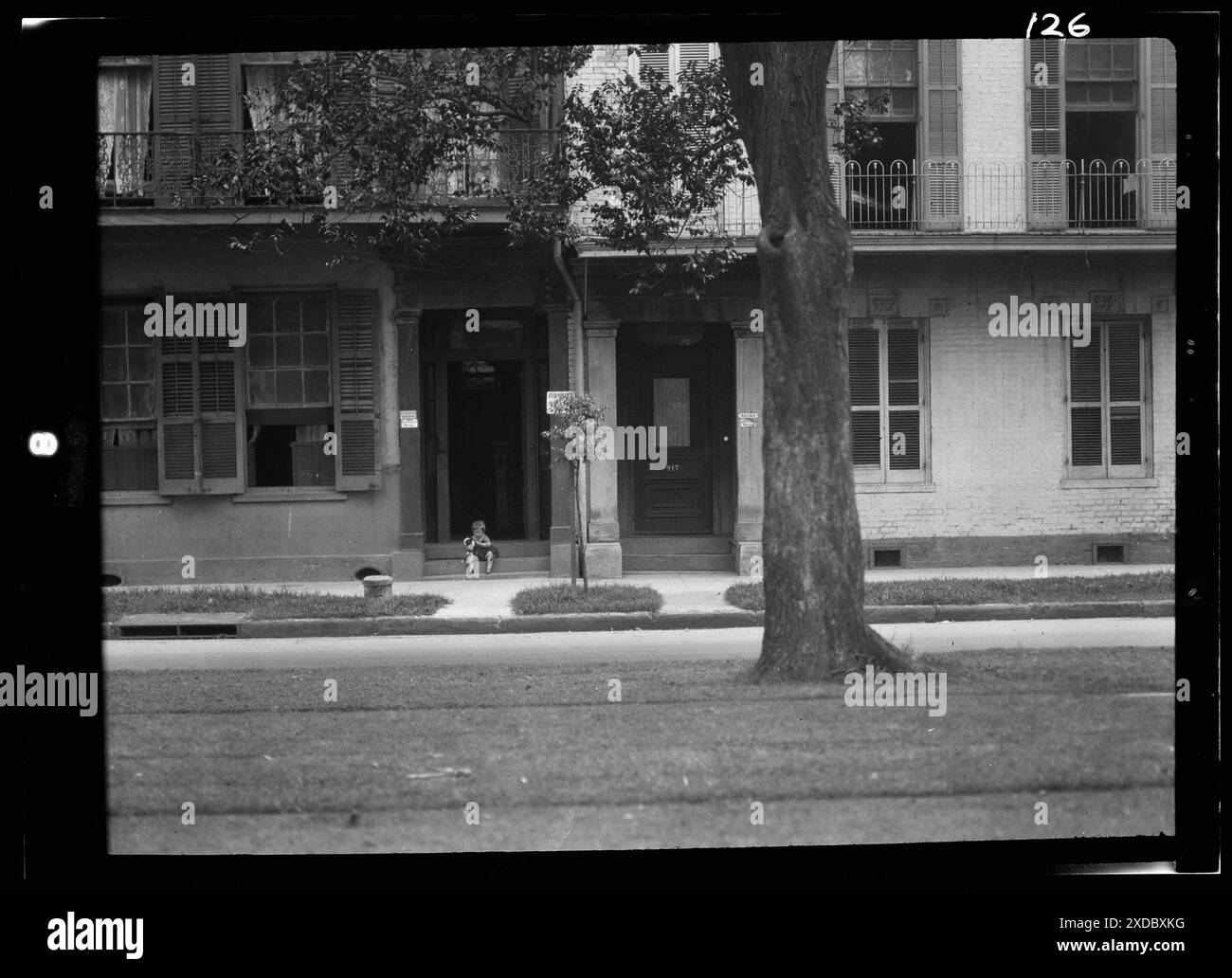 Child holding a dog sitting on steps of a boarding house, New Orleans