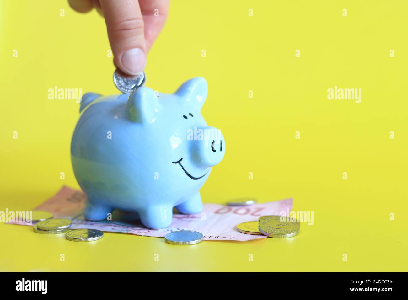 Woman's hand puts a coin into a piggy bank. Piggy bank on a yellow ...
