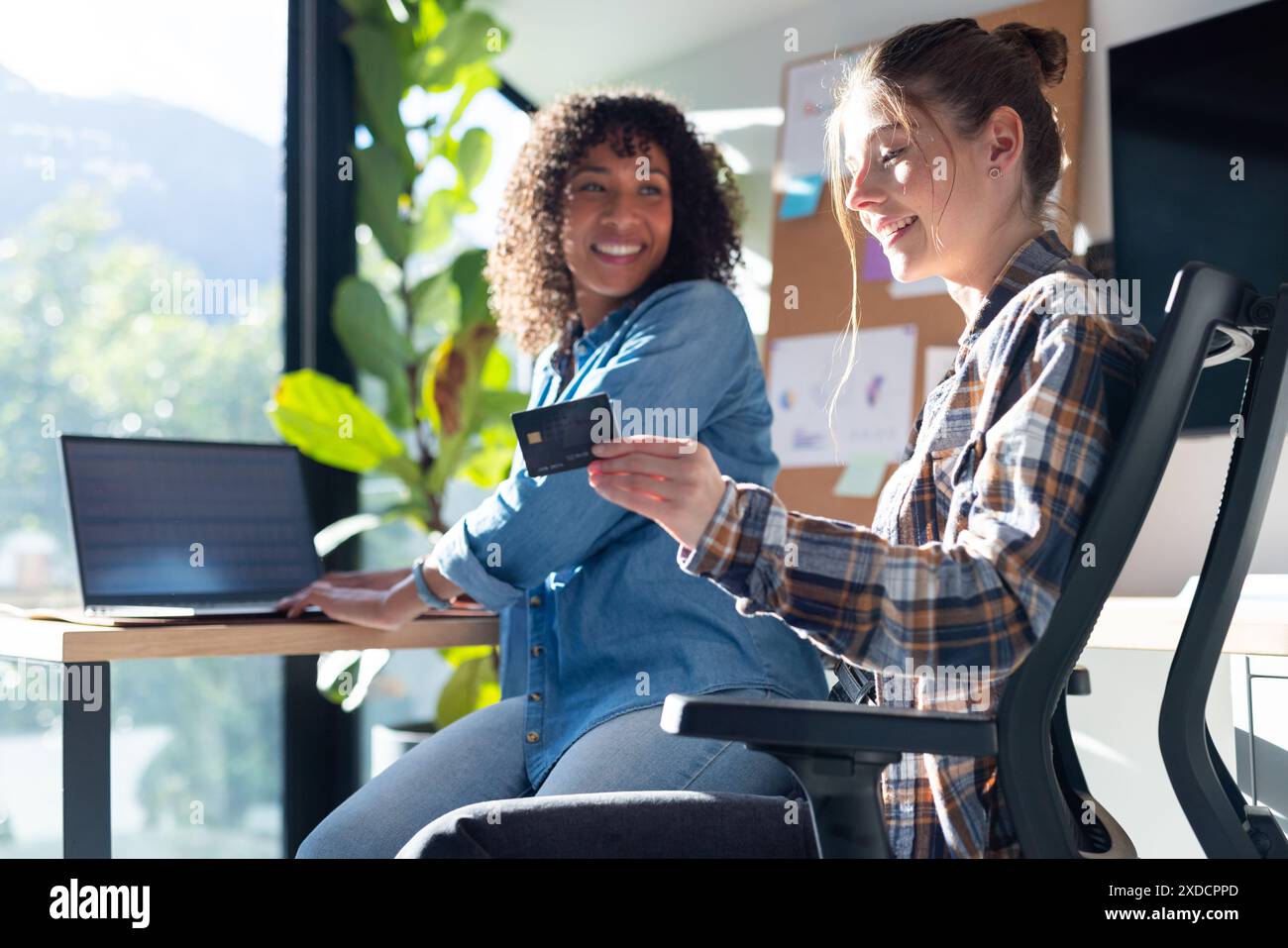 Sitting at desk, two women are using laptop and holding a credit card Stock Photo