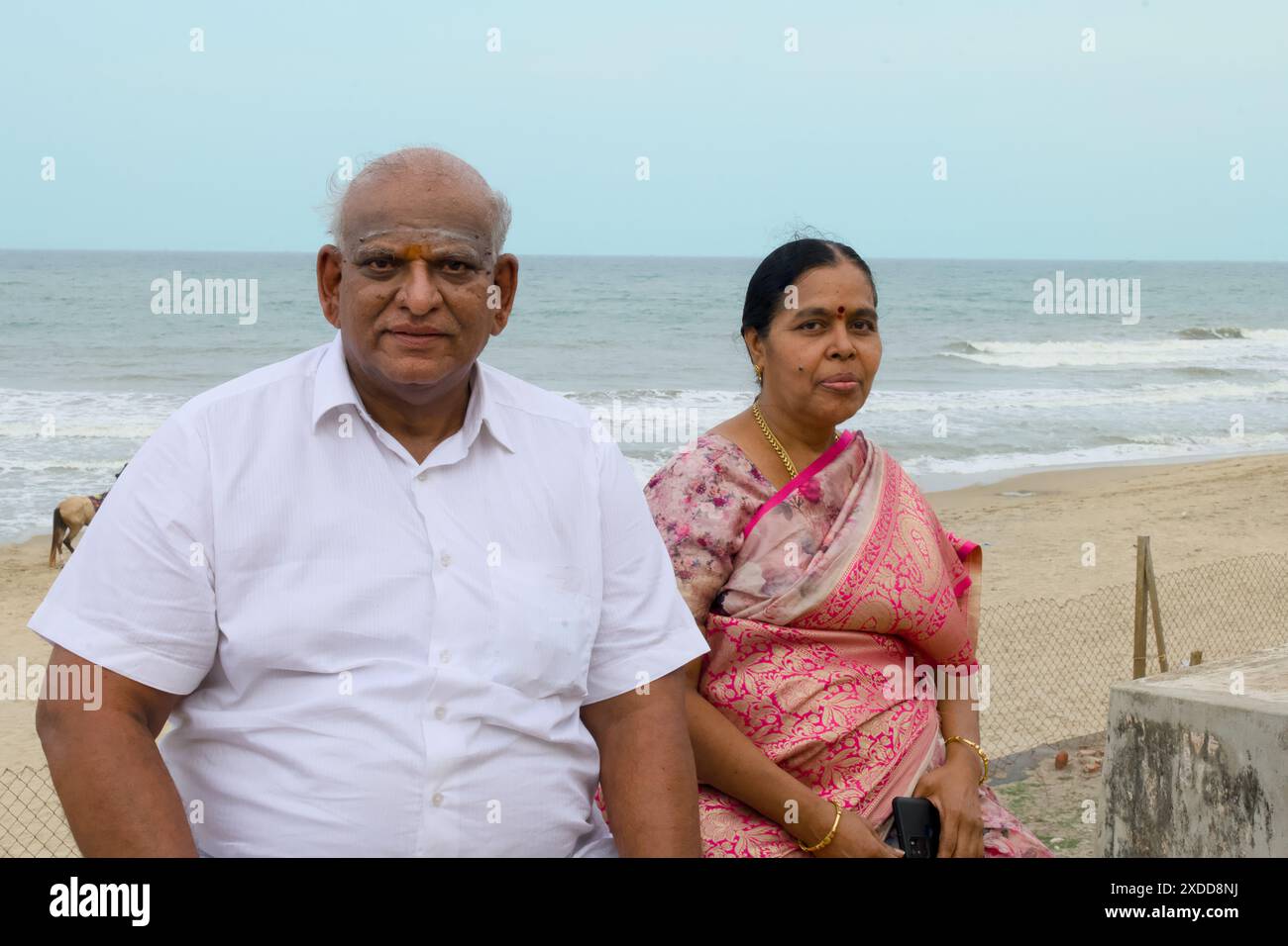 An Indian couple, adorned in traditional attire, shares quietude by the ocean��a timeless moment of love. Stock Photo