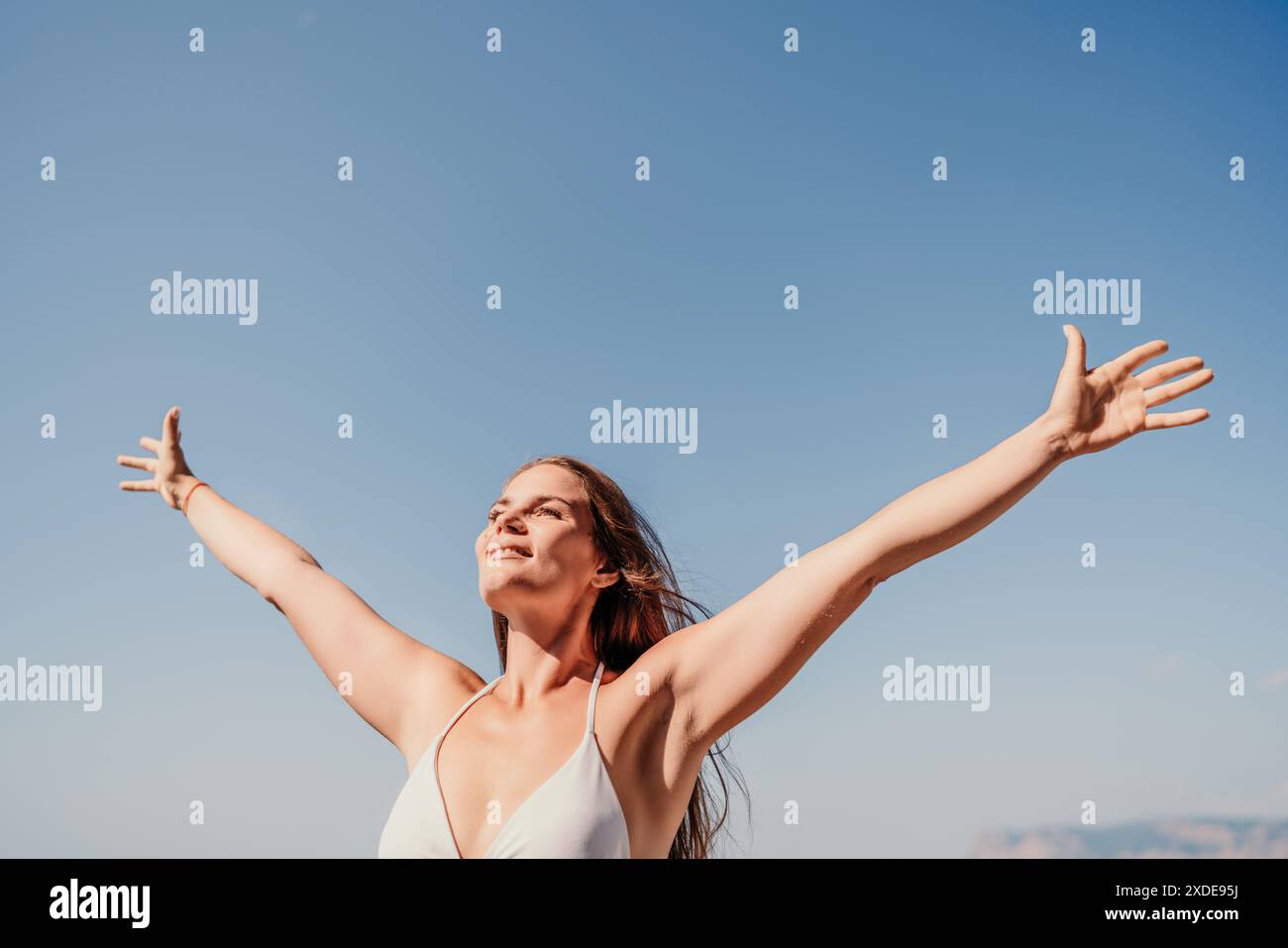 A woman is standing in the sun with her arms outstretched, looking up ...