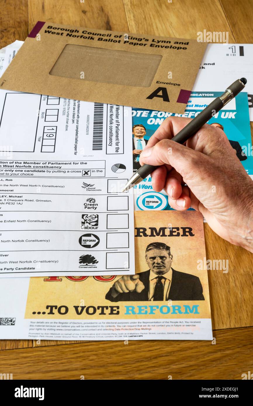 Woman completing a postal vote for the UK General Election 2024 with political parties campaign literature. Stock Photo