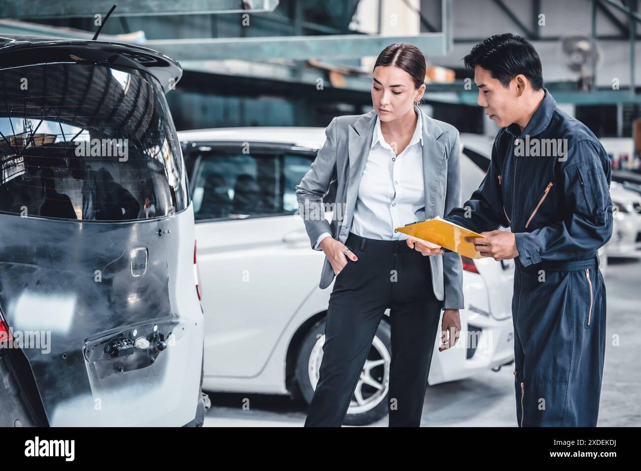 Mechanic working in a car repair shop is estimating the damage and cost of repairs with car owner. Stock Photo