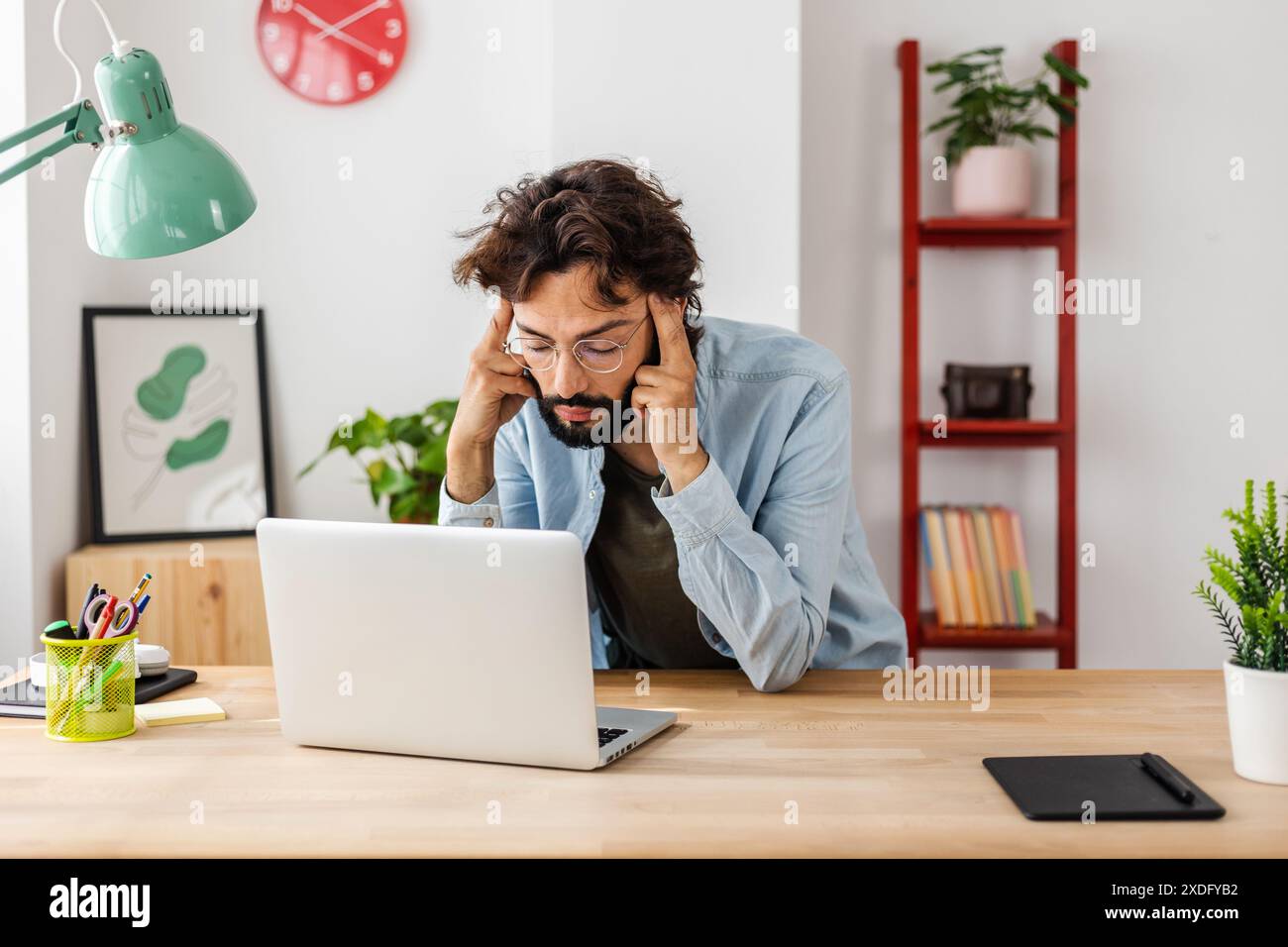 Exhausted man suffering from headache while working on his laptop. Stock Photo