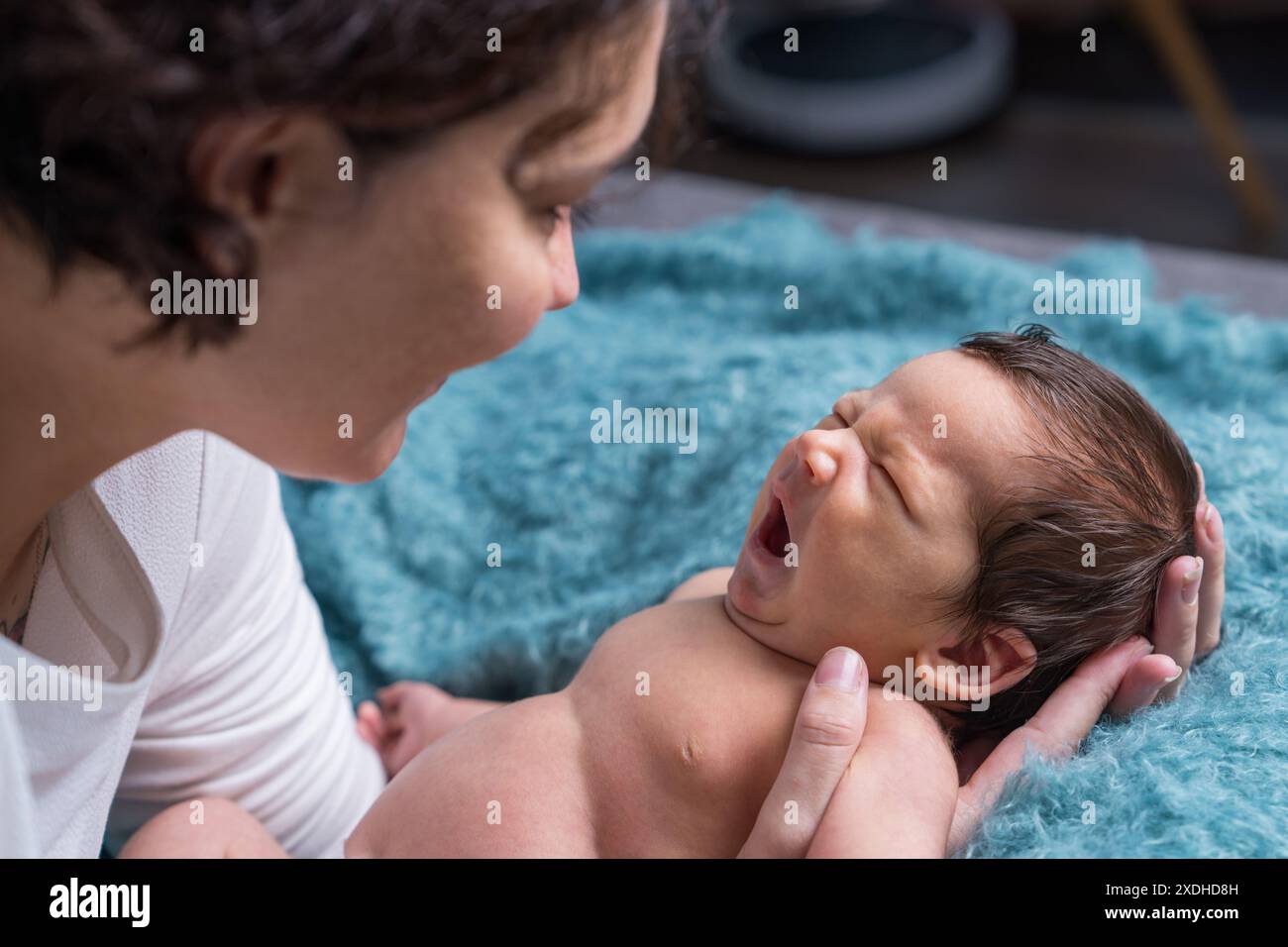 A loving mother takes care of her newborn baby. portrait of a mother holding a crying baby in her arms. Mother hugs her little son. Stock Photo