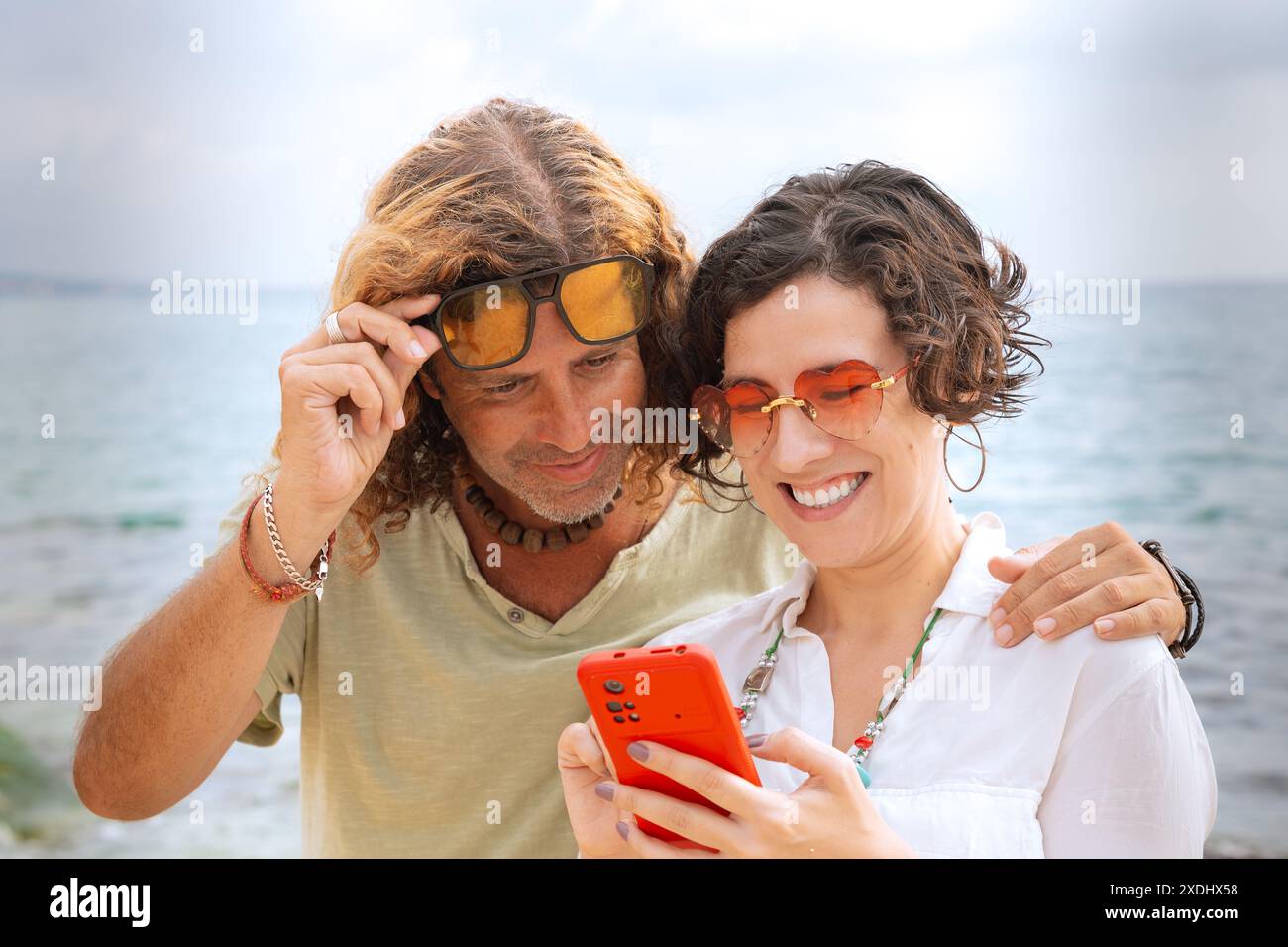 Smiling couple on the beach browsing smartphone apps. Stock Photo