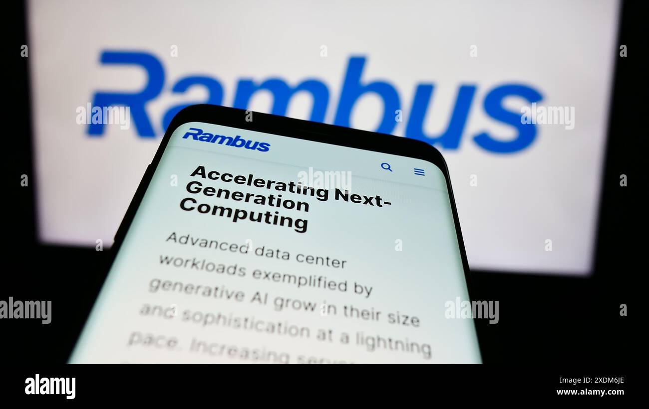 Smartphone with website of US semiconductor company Rambus Inc. in front of business logo. Focus on top-left of phone display. Stock Photo