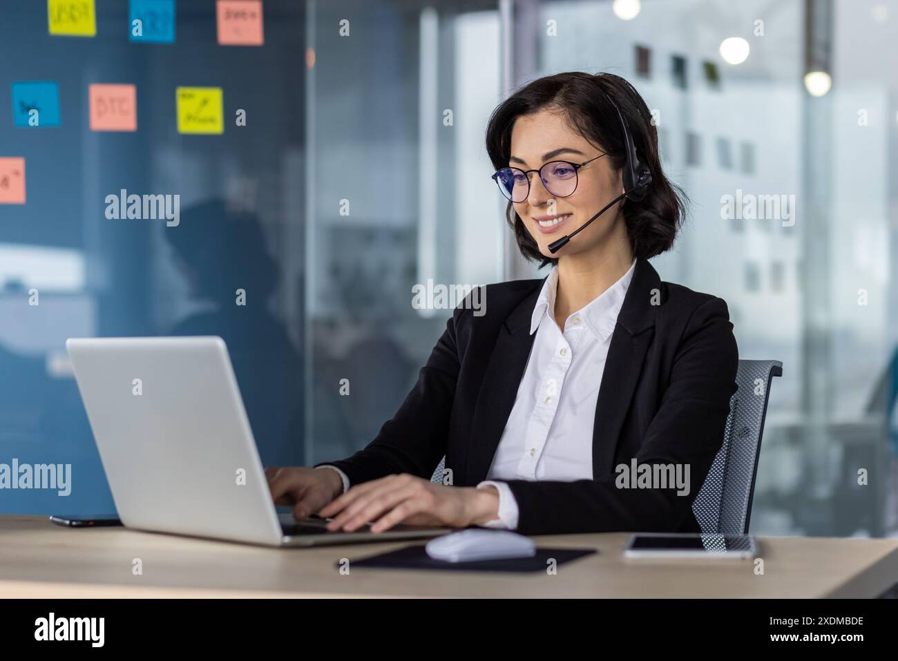 Businesswoman with headset working on laptop in a modern office. Ideal for concepts like customer support, business communication, and professional work environments. Stock Photo