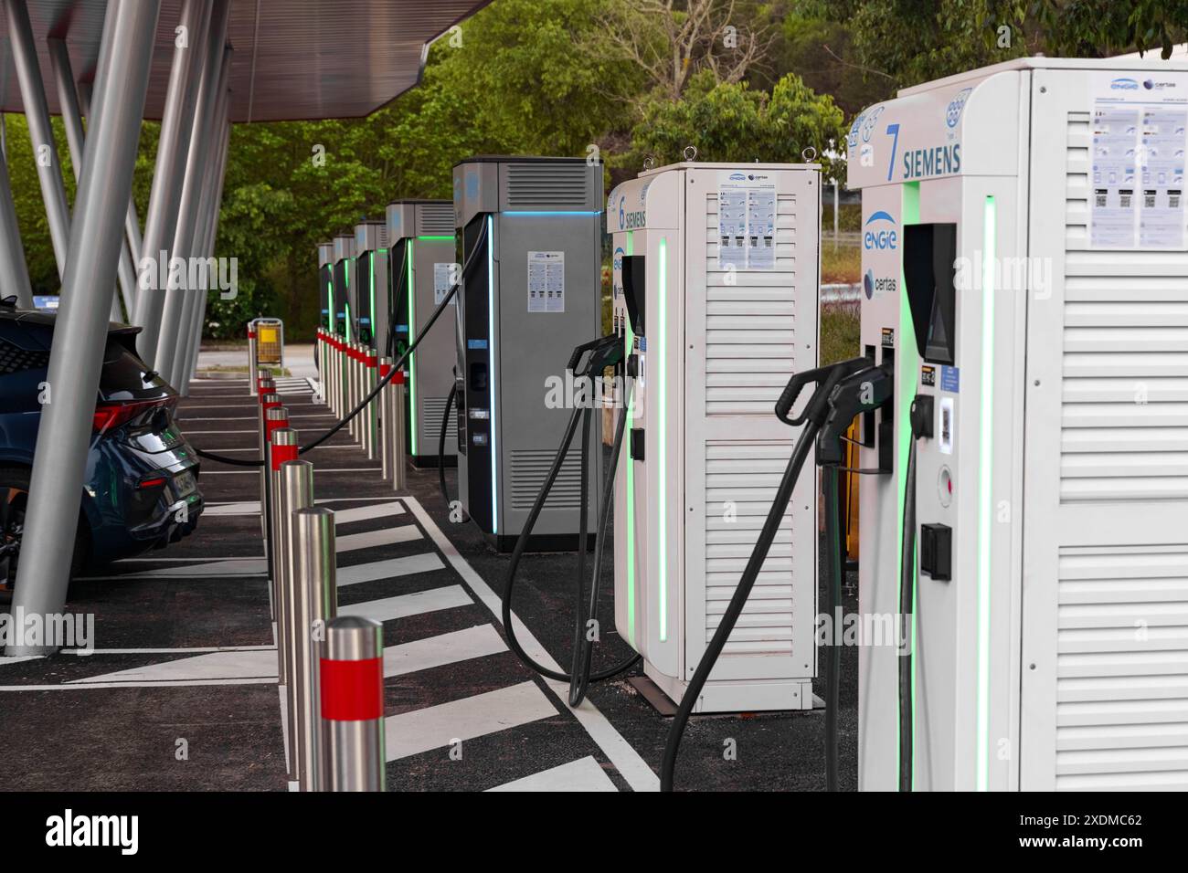 La Turbie, France - June 12, 2023: Multiple electric vehicle charging units lined up in an outdoor parking area, with cables connected to a parked car Stock Photo