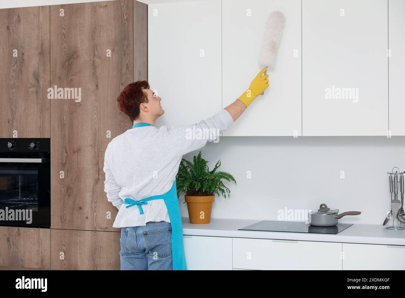 Young man cleaning cupboards with pp-duster in kitchen Stock Photo