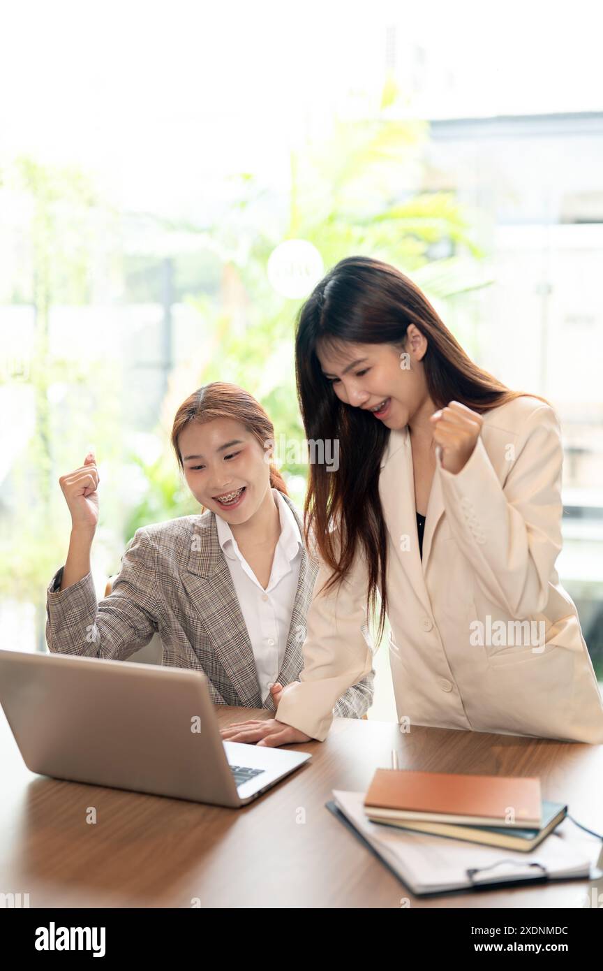 Two cheerful Asian businesswomen are celebrating their business project ...