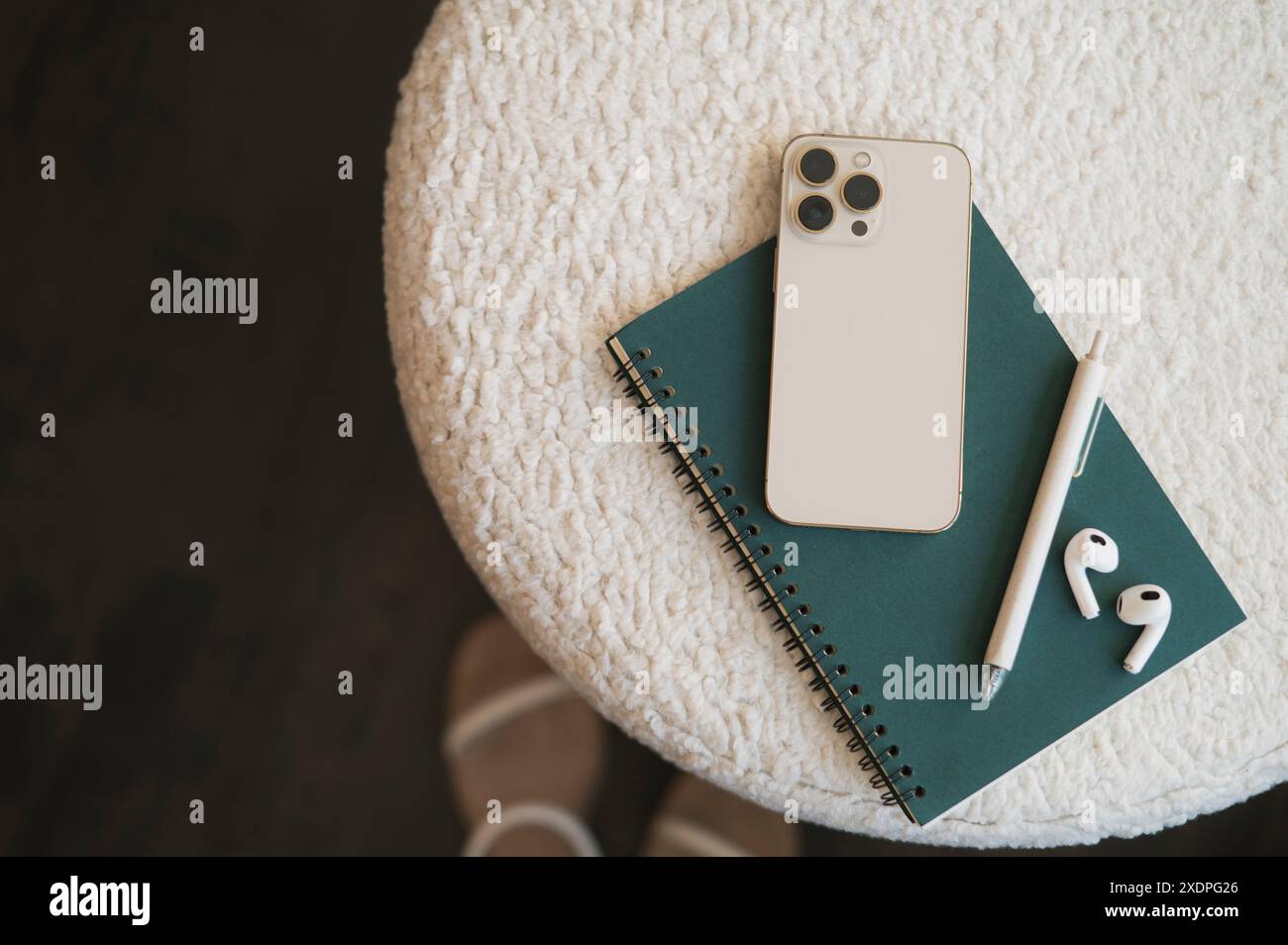 Smartphone, notebook, pen, and earbuds on a textured white surface. Stock Photo
