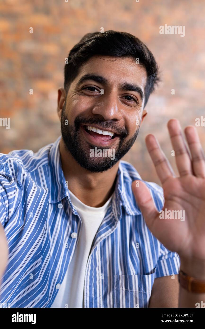 Smiling man waving at camera in casual shirt, engaging in video call Stock Photo