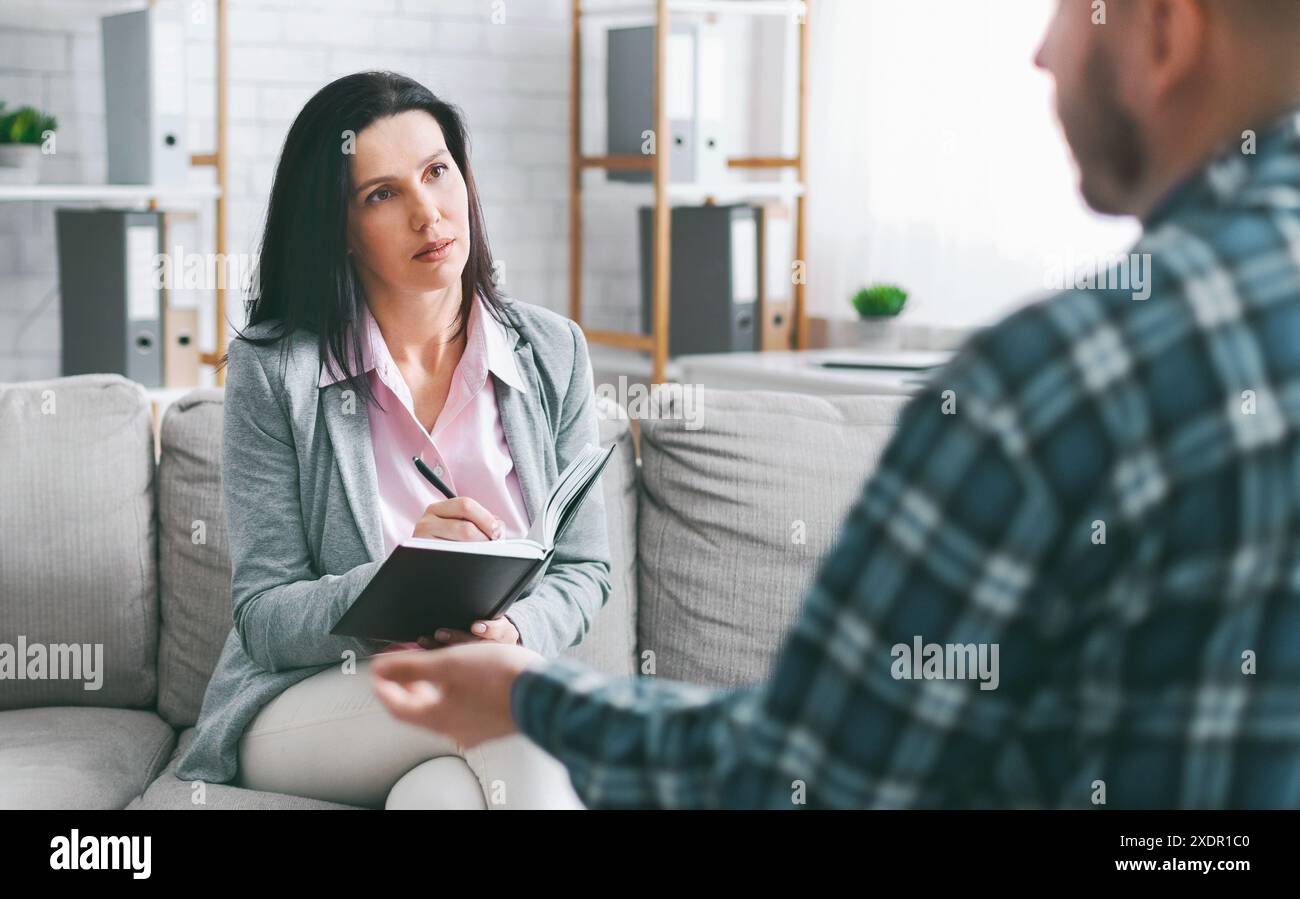 Woman Taking Notes During Therapy Session With Bearded Man Stock Photo