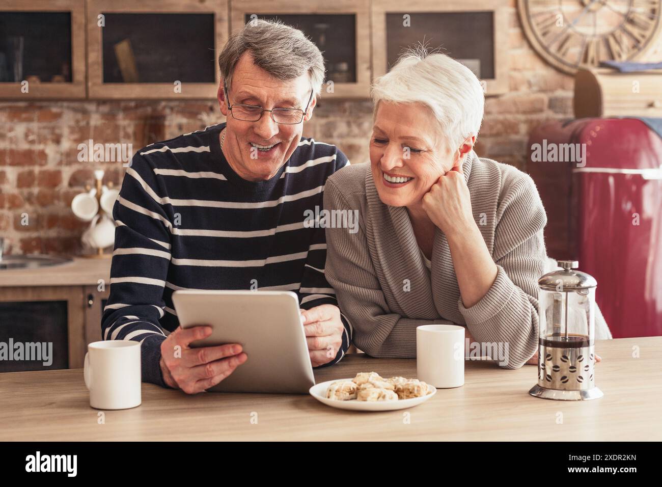 Senior Couple Laughing While Using Tablet Computer in Kitchen Stock Photo