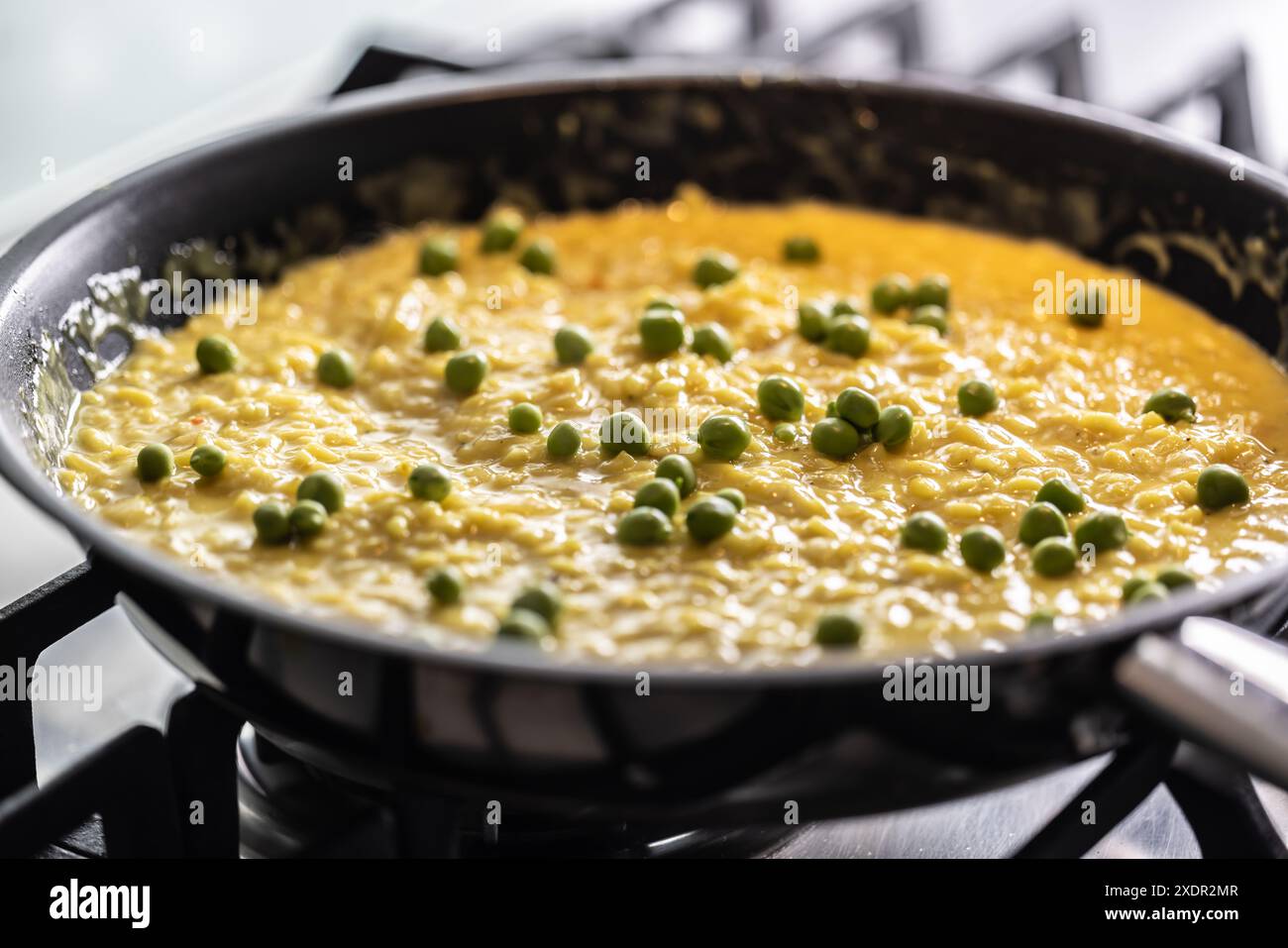 Saffron risotto with peas cooked in a pan on a gas stove. Stock Photo