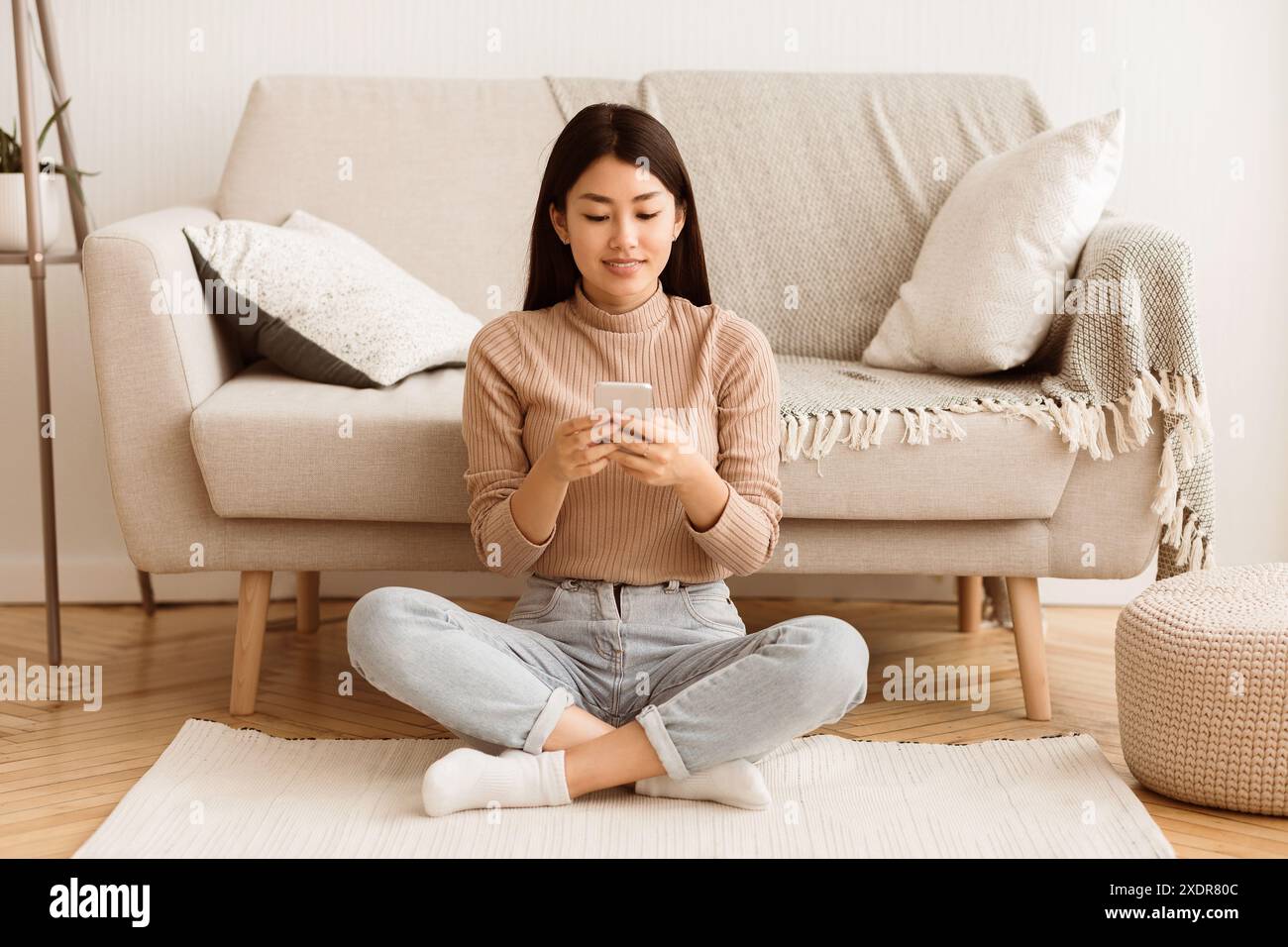 Woman Using Smartphone While Sitting On Floor Stock Photo