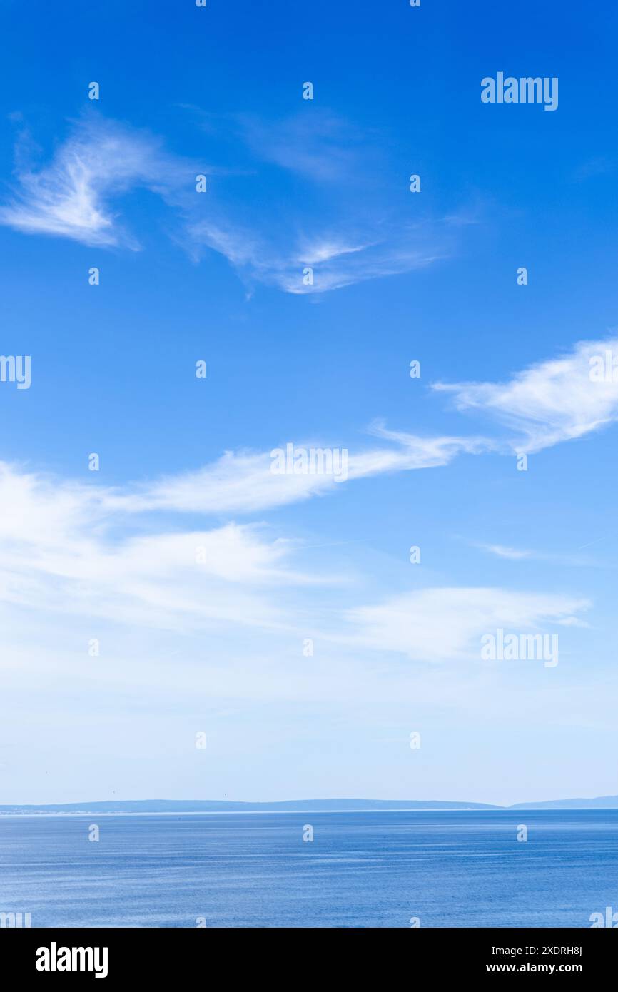 clear blue sky with thin, wispy white clouds above a calm, still ocean ...