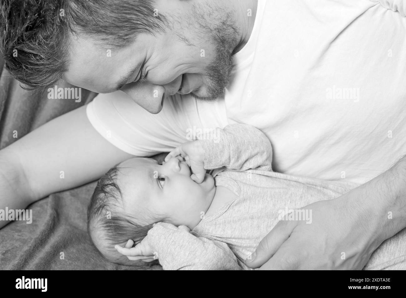 Black and white photo of father lying with his happy newborn baby boy