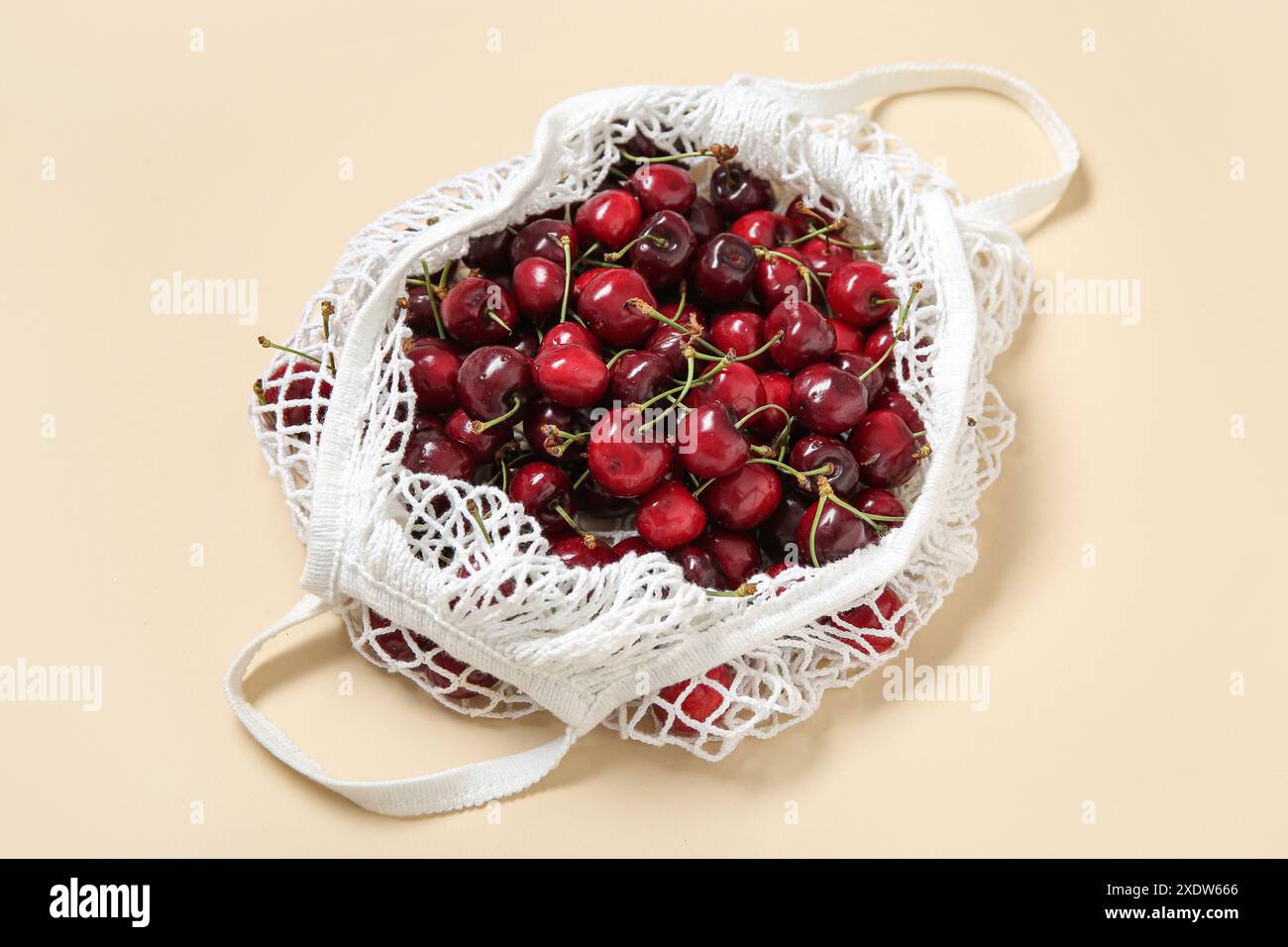 Mesh bag with fresh cherry on beige background, closeup Stock Photo