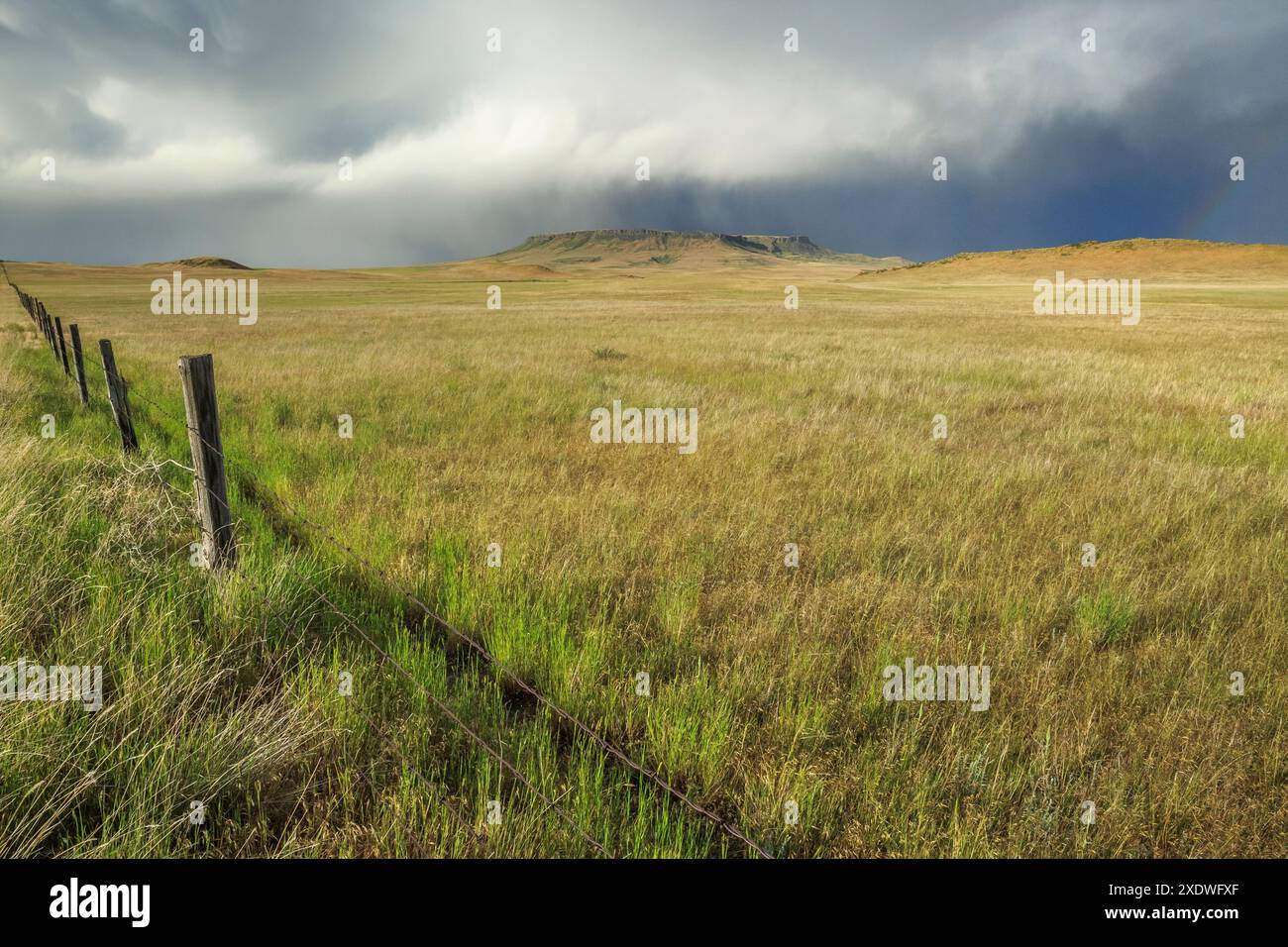 fence along the prairie below square butte during a passing rain storm ...