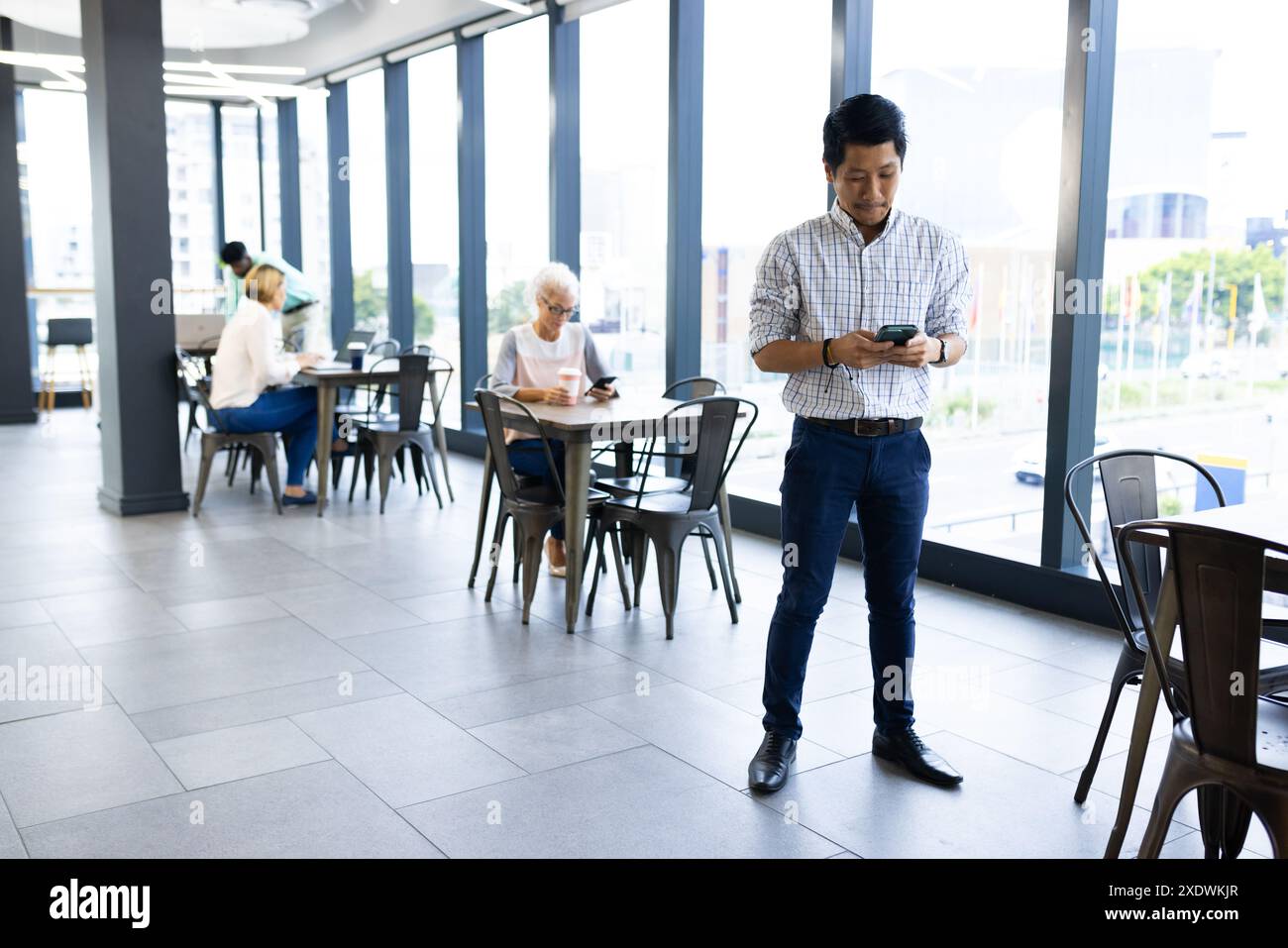 In office, man using smartphone while colleagues working at tables in background Stock Photo