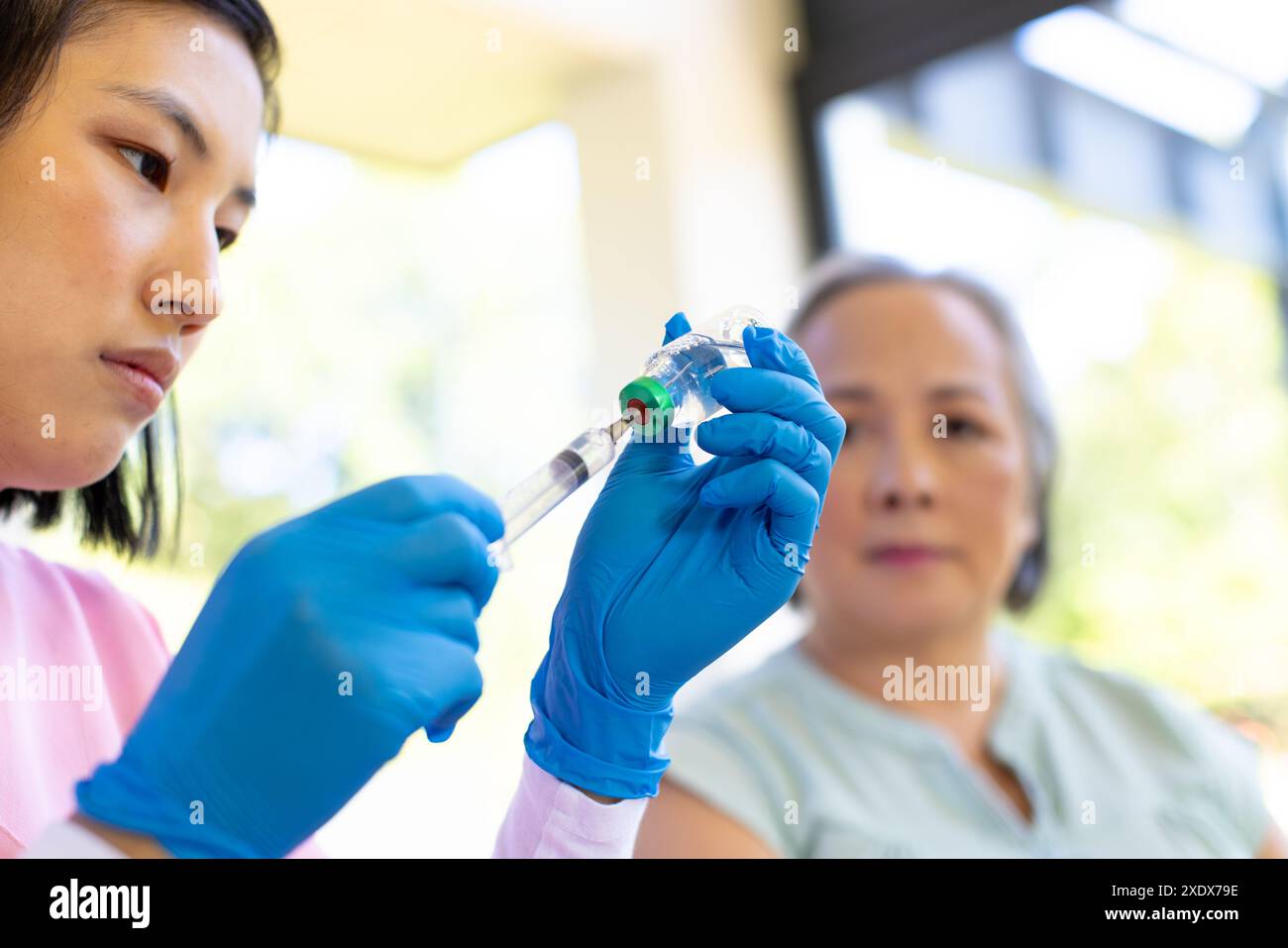Female nurse preparing syringe for senior woman during home visit for medical care Stock Photo