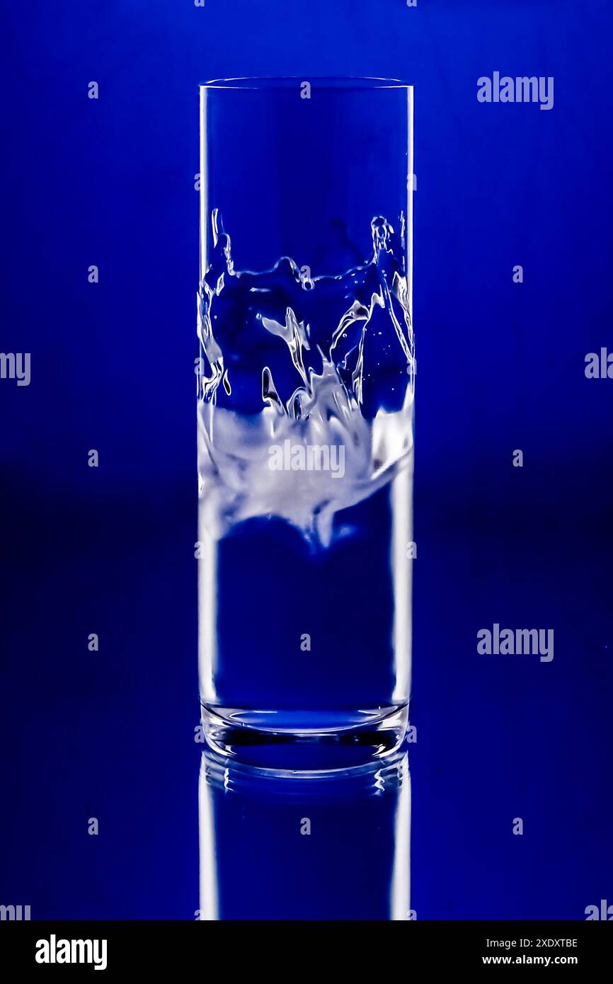 Traditional Turkish Raki glass with an artistic and dynamic splash of water inside, set against a vibrant blue background. Stock Photo