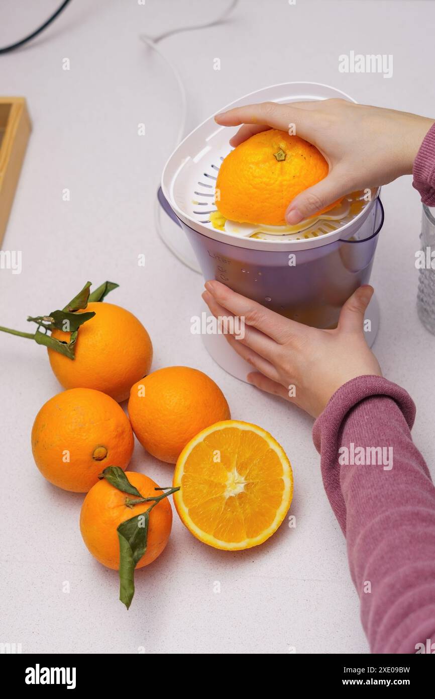 Woman's hands squeezing oranges in a juicer Stock Photo