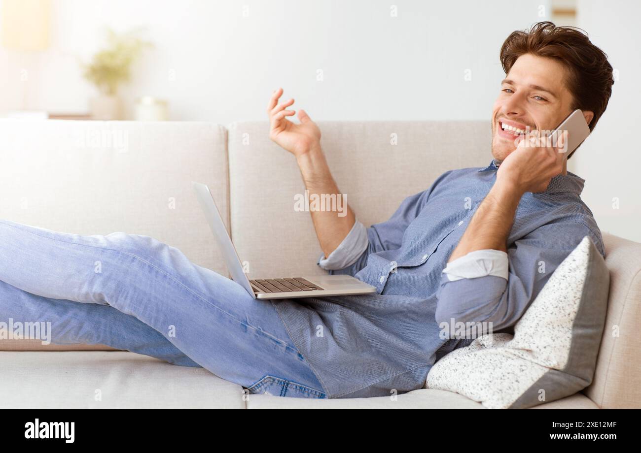 Man on Couch Talking on Phone With Laptop Stock Photo