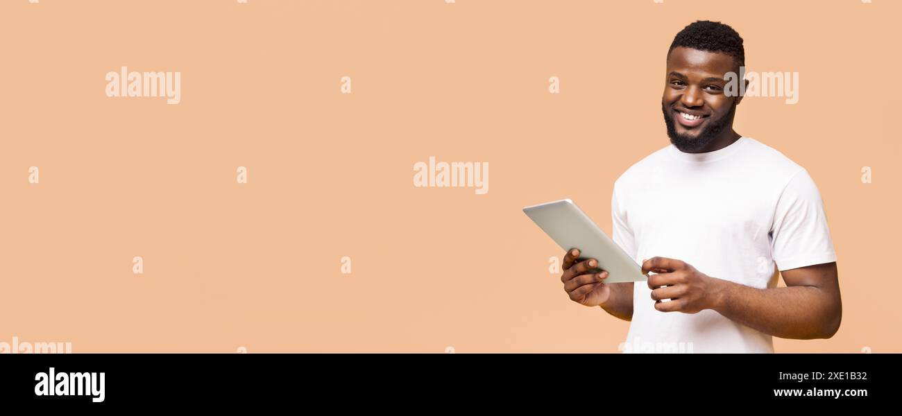 Smiling Man Using Tablet in Front of a Peach Background Stock Photo