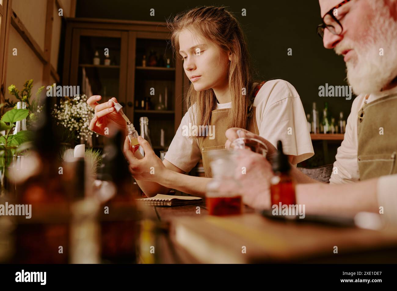 Perfumer Assistant Mature perfumer mixing aromatic liquid while his young female assistant ...