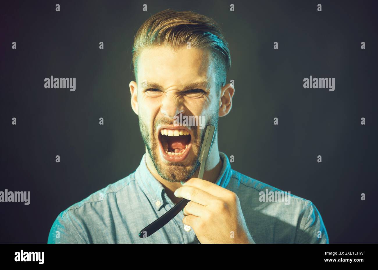 Barbershop. Professional hairdresser with straight razor. Angry barber with dangerous razor. Handsome screaming bearded man in denim shirt with Stock Photo