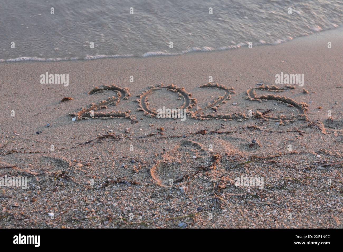 New Year 2025, lettering on the beach. Numbers 2025 year on the sea shore, message handwritten in the golden sand on beautiful beach background. Stock Photo