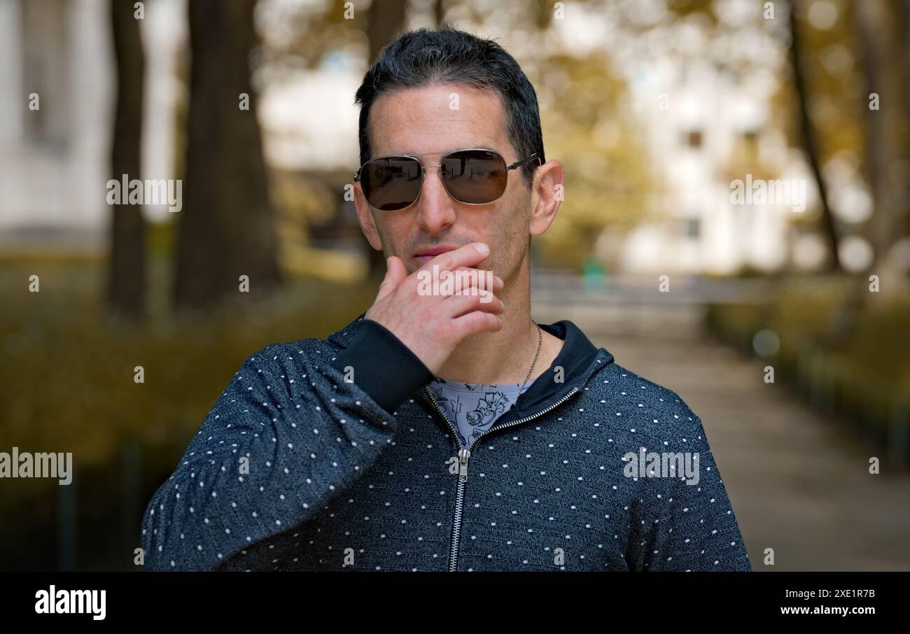 Mediterranean man in casual sports clothing and sunglasses, focused attitude with a hand on the face. Stock Photo