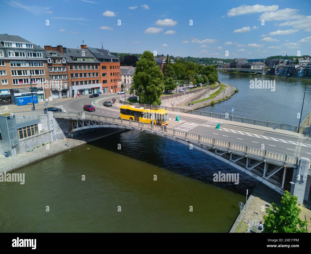 Yellow bus crossing a bridge over Sambre river in Namur, Belgium, on a sunny day. Aerial view. Stock Photo