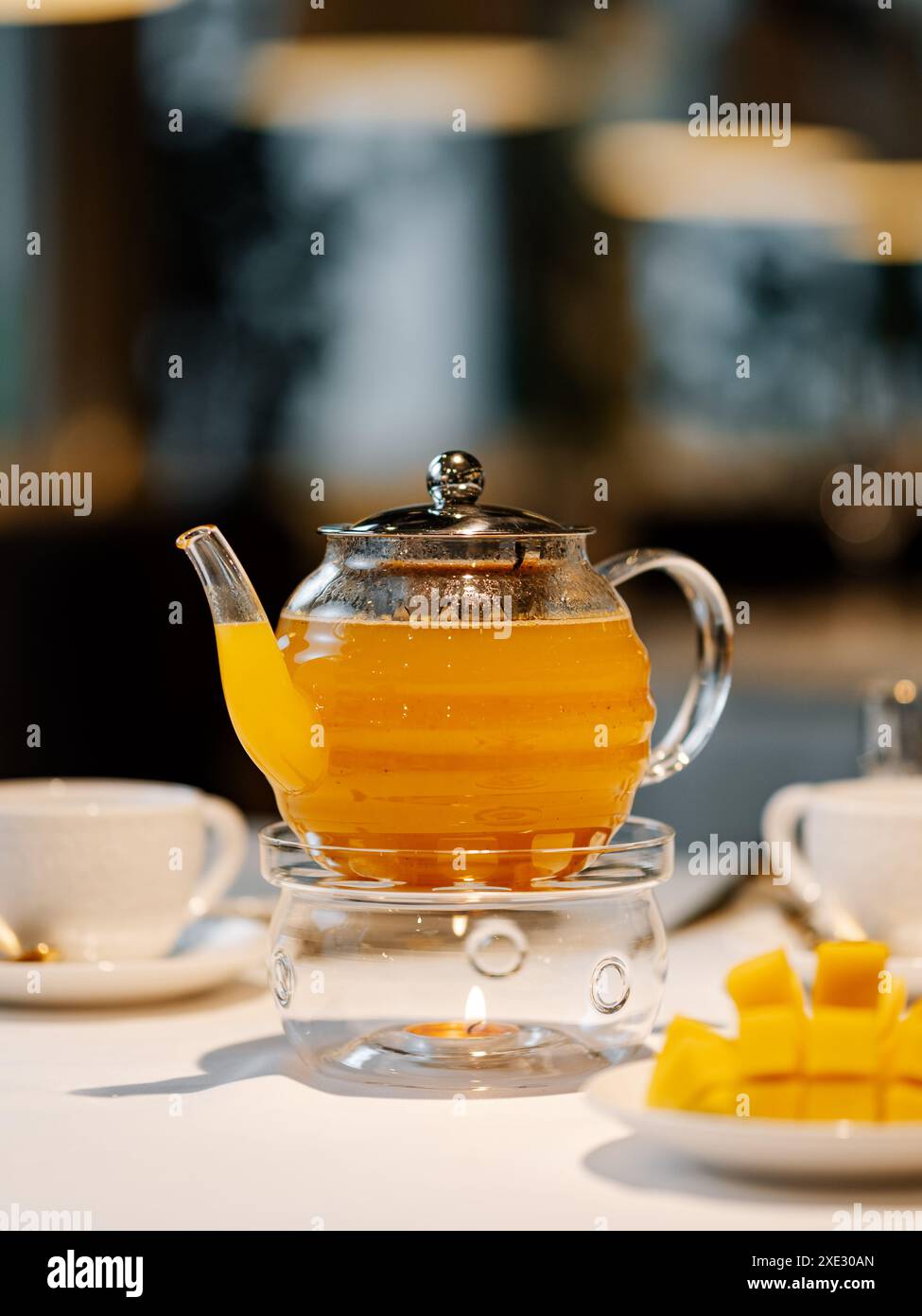 Mango herbal tea in teapot with warmer on table Stock Photo