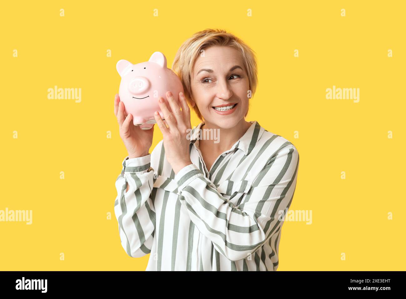 Happy mature woman with piggy bank on yellow background Stock Photo - Alamy