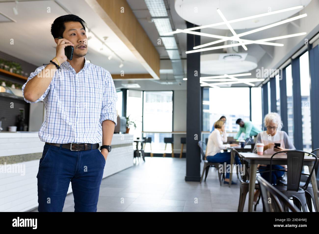 Talking on smartphone, man standing in modern office with colleagues working Stock Photo