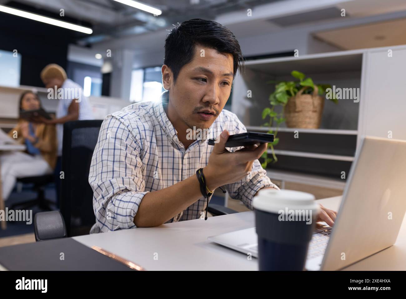 Using smartphone for voice command, man working on laptop in office Stock Photo