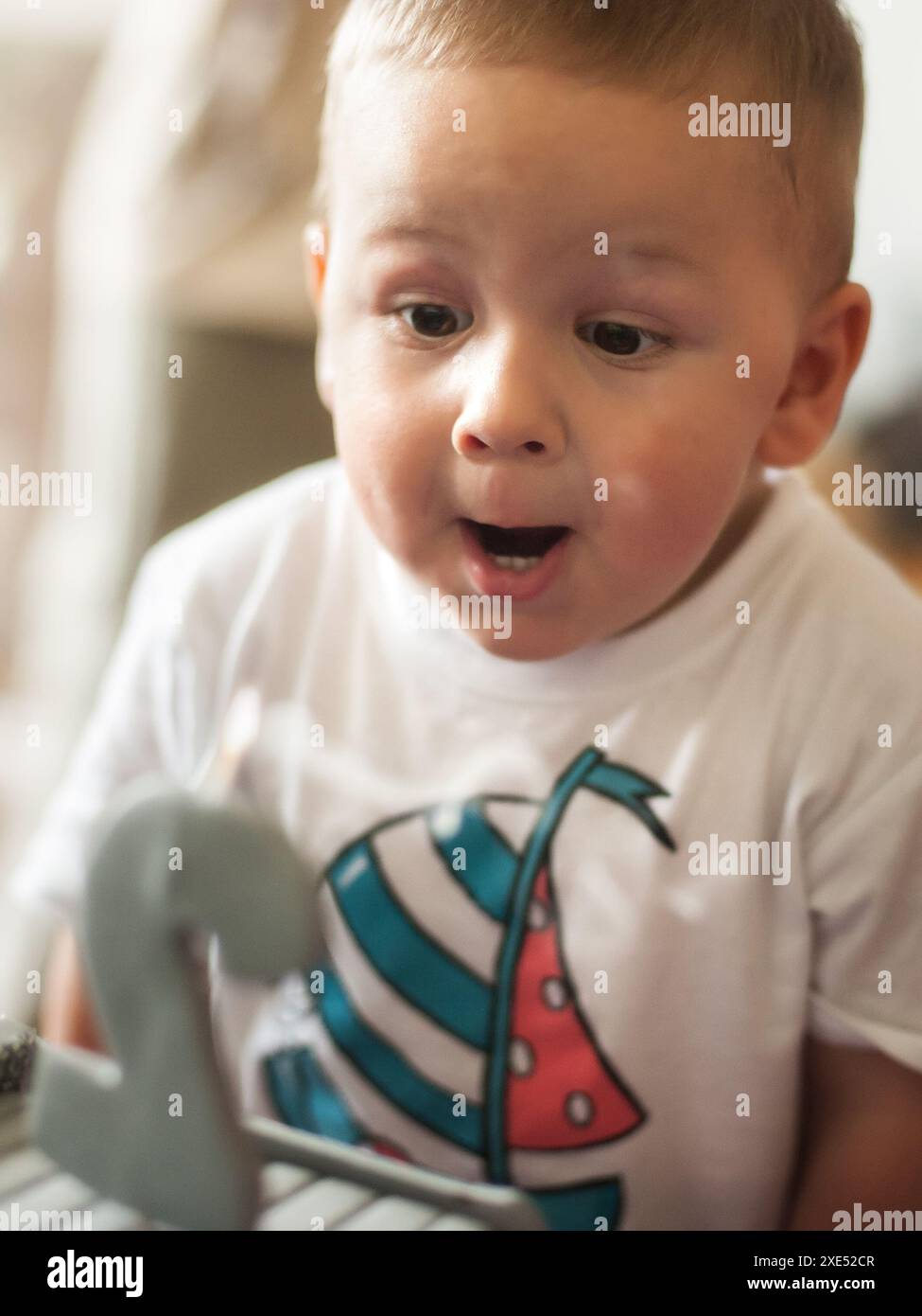 Cute happy two year old boy blowing out candles on his birthday on a big, delicious cake in the shape of a truck. Celebrating birthday party for kids Stock Photo