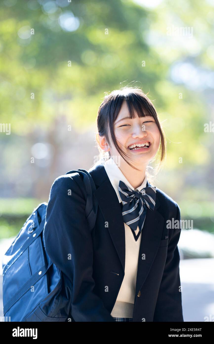 Schoolgirl in school uniform smiling with greenery in the background ...