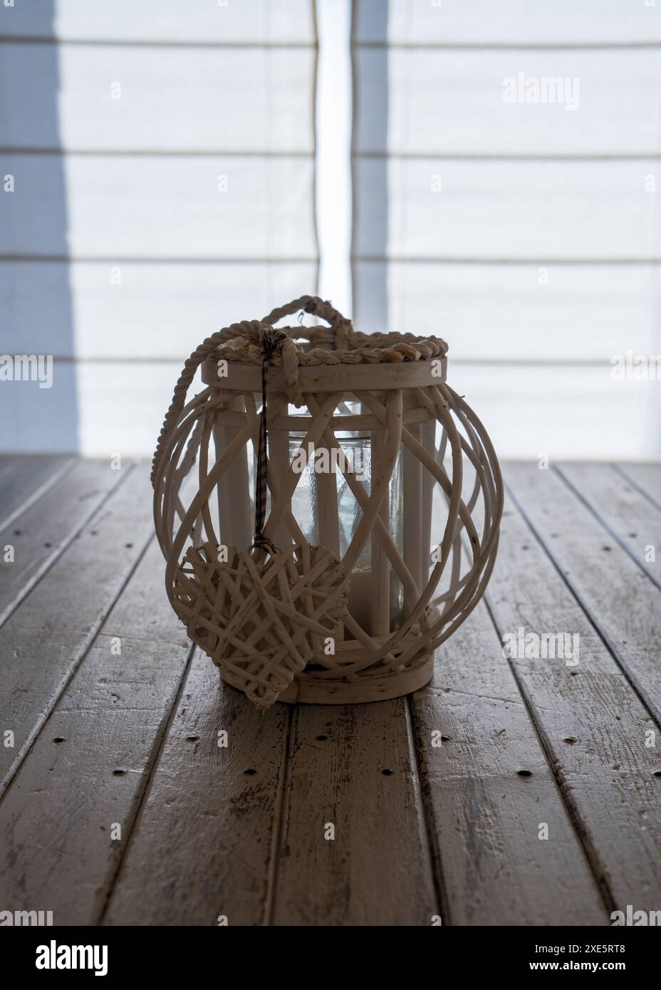 A wicker wooden candlestick with a heart stands on a wooden table against a white wooden wall. Table decoration, decoration Stock Photo