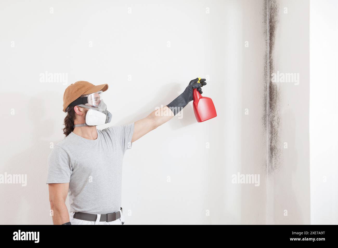 Man worker spraying product on wall to remove mold, wearing protective