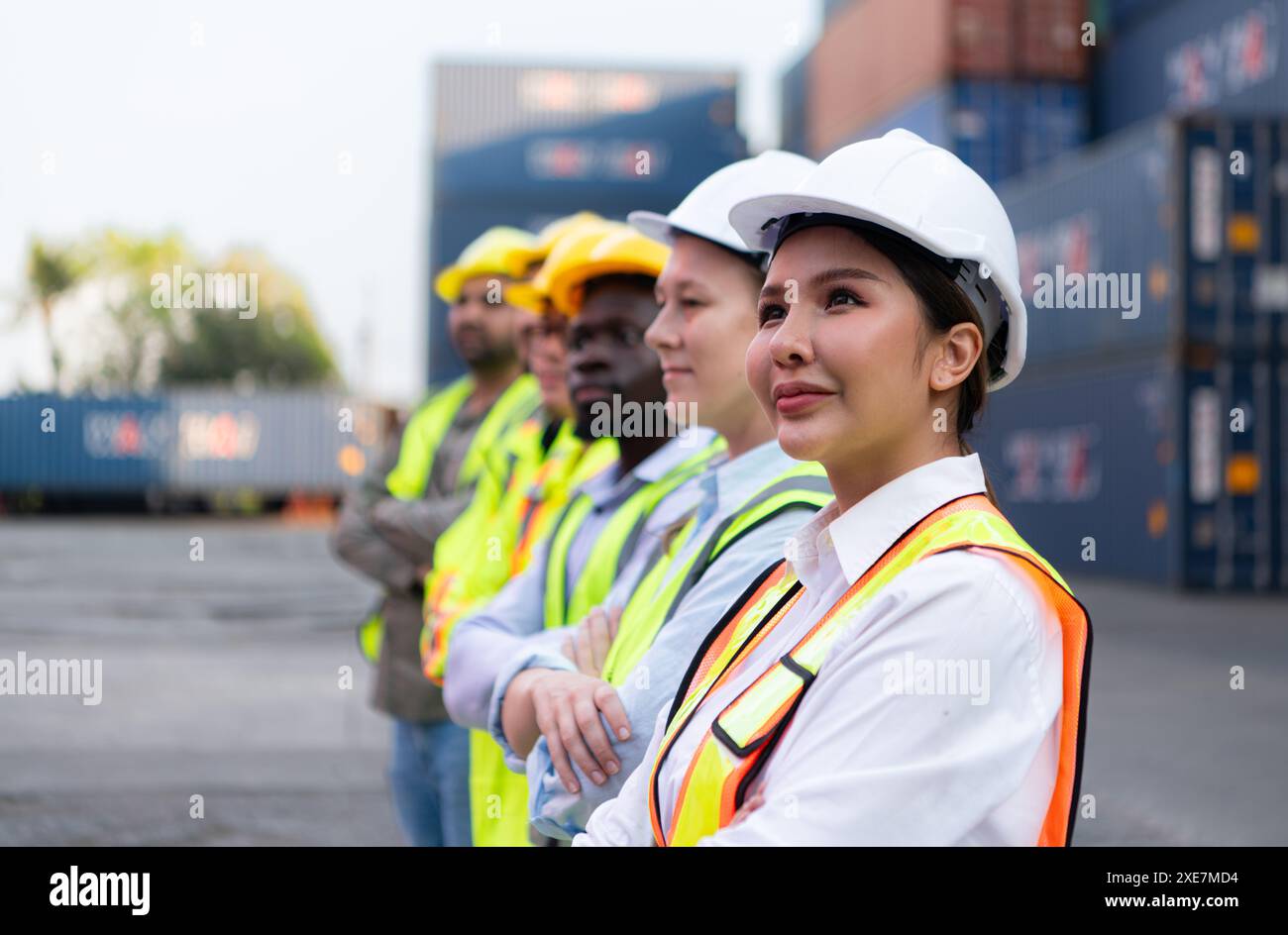 Group of worker wearing safety helmet and reflective vest standing in front of containers. Stock Photo