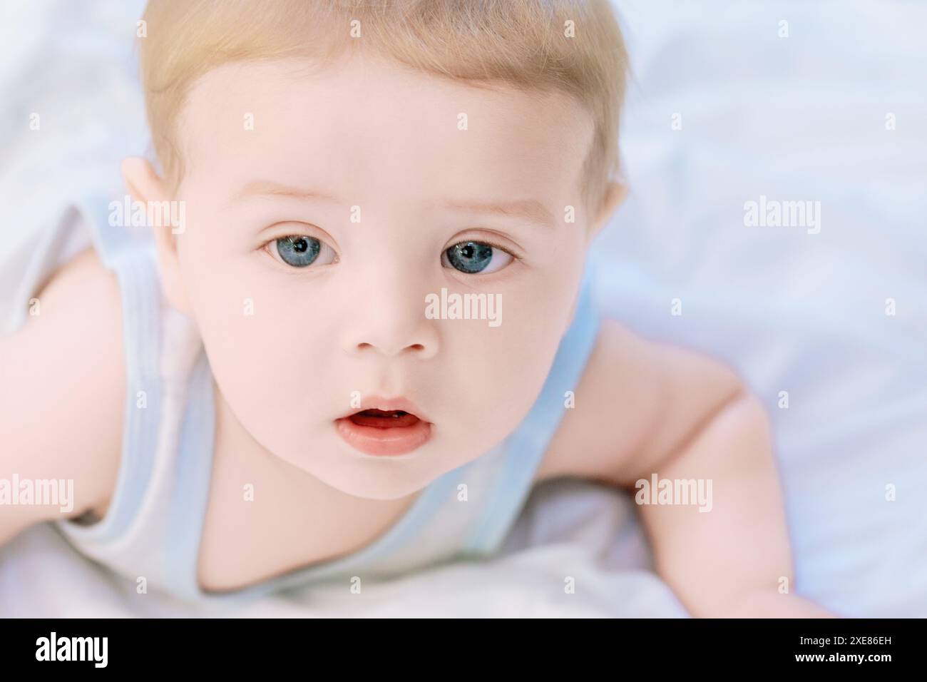 Cute baby boy with blonde hair and blue eyes lies peacefully on a white ...