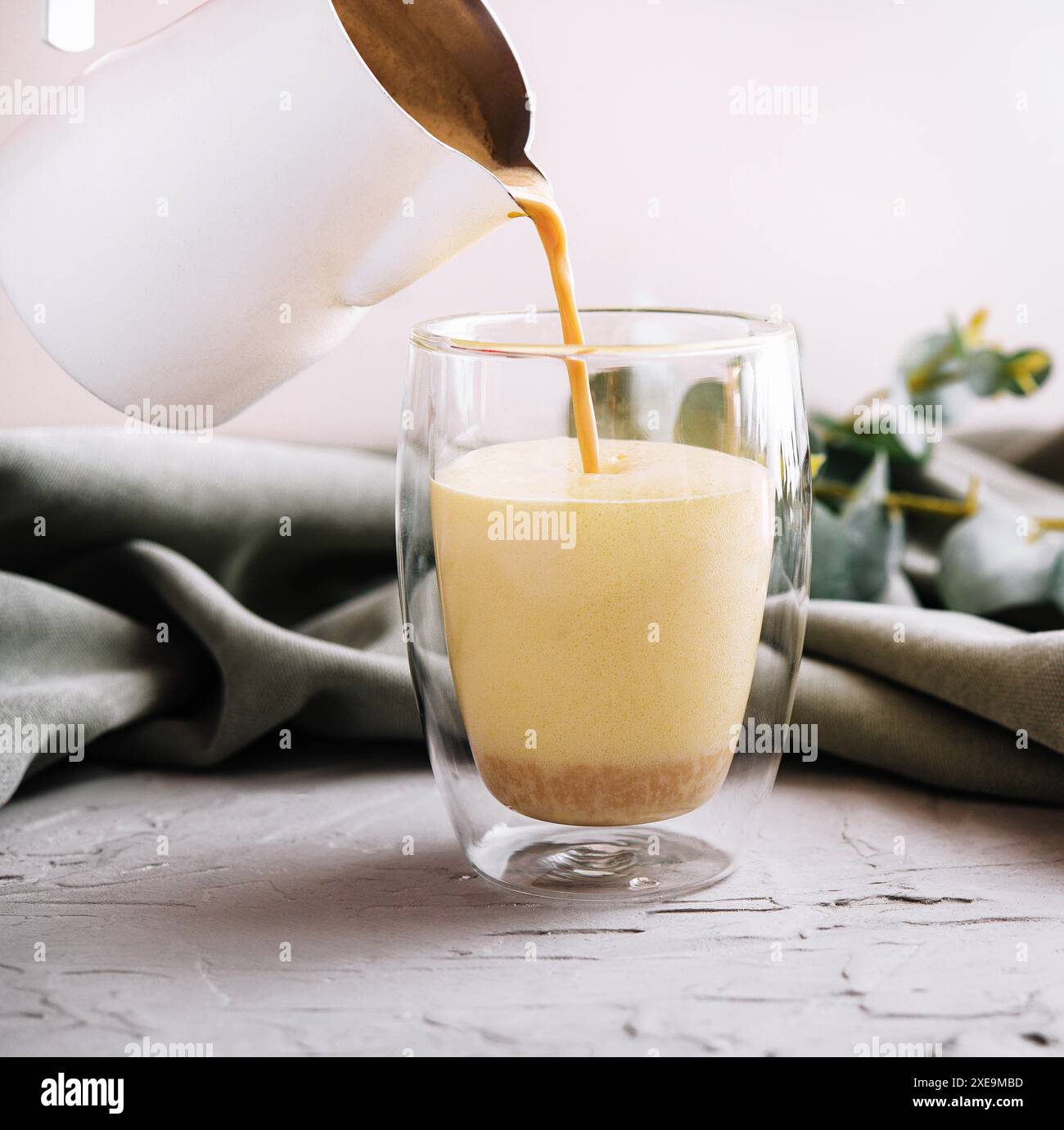 Pouring a coffee with milk from teapot to glass cup Stock Photo