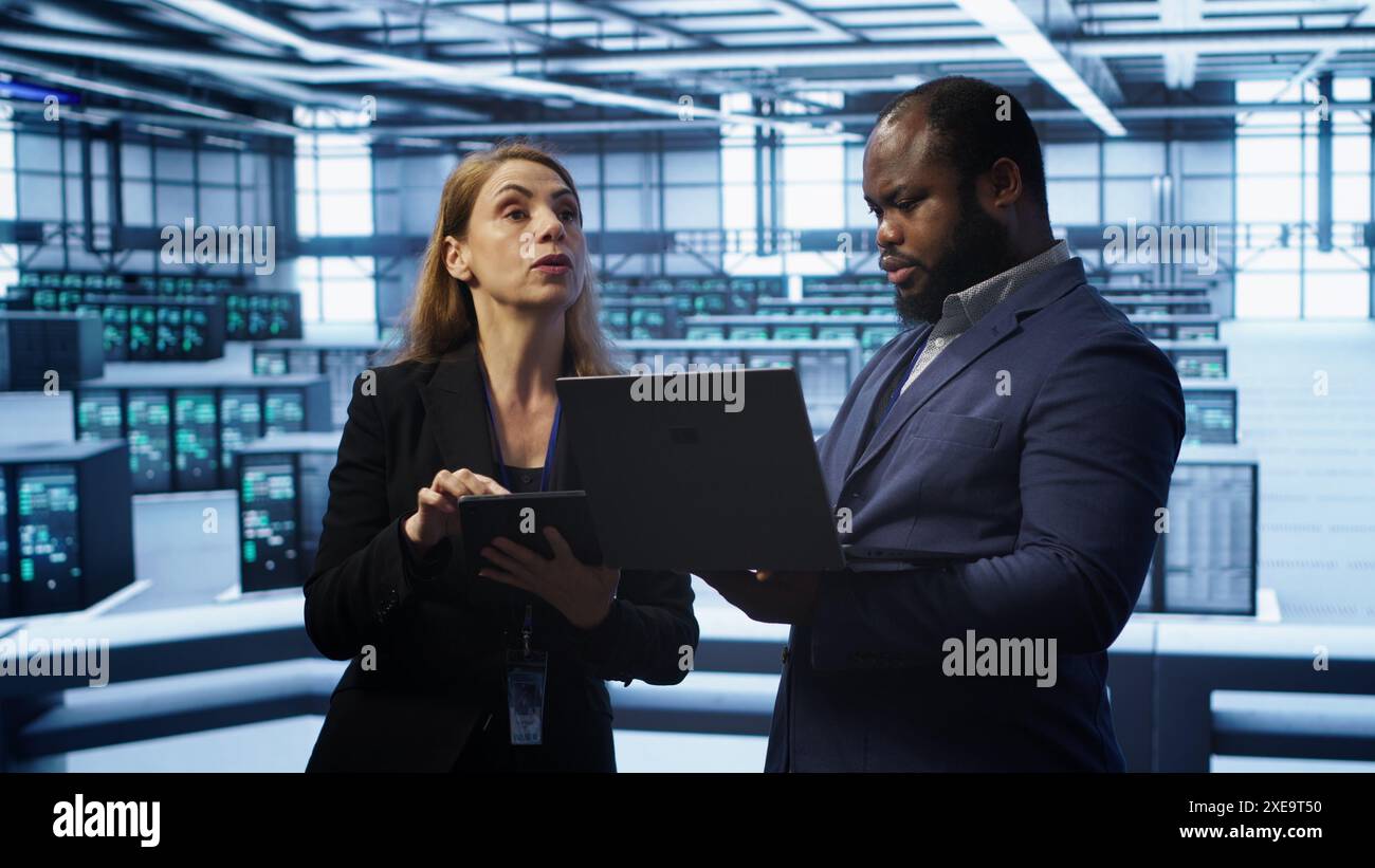 Manager in data center supervising worker running error checking utilities to fix errors. Supervisor in server farm overseeing engineer repairing network issues affecting rigs performance, camera A Stock Photo