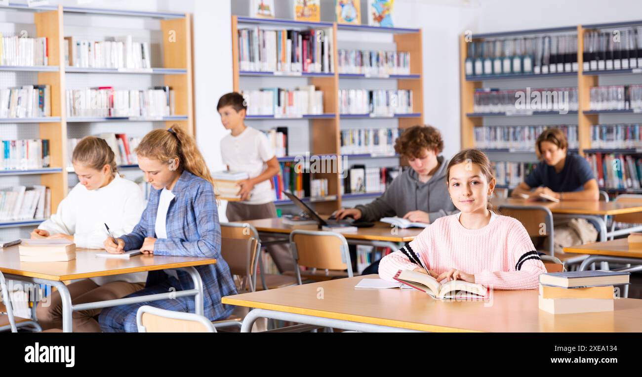 Portrait of preteen girl reading books in college library Stock Photo ...